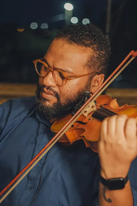 Violinista de óculos e barba tocando à noite, ao ar livre